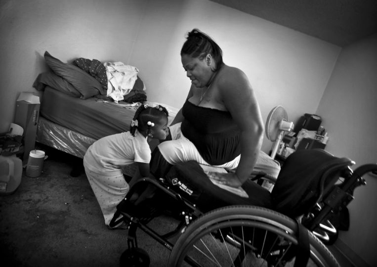 Rose Smith was shot on her front doorstep in a South Los Angeles housing project, caught in the crossfire of rival gangs.  With two young children and a baby on the way, when  the bullets tore through her arms, broke her jaw, and left her paralysed from the waist down, she thought God, please don't let me die right now. --It's not my time to go--.  In the ensuing months she was in constant pain, spending most of her days in bed.  She named her baby --Miracle.-- Now three years old, Miracle lifts her mother's leg as Rose slides into her wheelchair.  --We both really are a miracle-- says Rose --because we both survived that shooting.-- The family had stem cells from Miracle's umbilical cord preserved in hopes that doctors may one day use them to help restore feeling in Rose's spine. © Barbara Davidson / Los Angeles Times