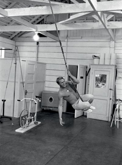 Steve McQueen swinging from rope at gym, 1963 © John Dominis