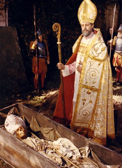Jean Distinghin. L'évêque mort et l'évêque vivant (Claudio Brook). Photographie couleurs réalisée lors du tournage du film de Luis Bunuel La voie lactée, 1969. (Décors par Pierre Guffroy, costumes par Jacqueline Guyot). Tirage chromogène d'époque 29,7 x 23,5 cm. Au verso du tirage, tampon Archives Maurice Bessy. rnProvenance : Collection Maurice Bessy. rnAu cours de cette séquence du film, le corps d'un évêque canonisé était exhumé. Mais on constata que ce dernier était hérétique et il fut alors excommunié.rnBunuel --revisitait-- ici les évêques vivants et morts qu'il avait mis en scène dans L'Age d'or en 1930.rn