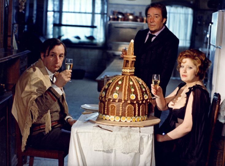 Bernard Prim. Andréa Ferréol, Ugo Tognazzi, Philippe Noiret, santé ! (autour du dôme des Invalides). Photographie couleurs réalisée lors du tournage du film de Marco Ferreri La grande bouffe, 1973. Tirage chromogène d'époque 23,5 x 29,2 cm. rnGénérer et créer sa propre mort, qui plus est par excès de nourriture quand une partie de l'humanité meurt de faim : cette démarche parut insupportable et inadmissible à beaucoup, et la sortie du film provoqua un scandale d'une rare intensité. Rarement le propos de Jean Cocteau Filmer c'est montrer la mort au travail fut autant illustrer par un film.