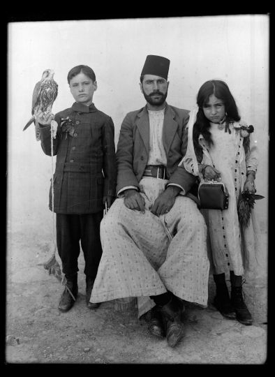 En Syrie, près de Palmyre, le maire du village de Qariateïn avec son fils, et sa fille, chacun des enfants tenant un objet symbolique de la masculinité ou féminité, le faucon, le sac à main de la maman. Janvier 1914. Photo : père R. Savignac, dominicain de Jérusalem