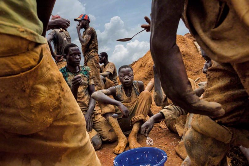 Miners eat lunch from a communal bowl in the mining town of Pluto in Ituri Province. They work here to extract rock and sand from a large pit that has taken over a year to excavate. The miners are made up of many different people from all over Congo who come to seek their fortune. Pluto, Democratic Republic of the Congo, 2013 © Photo by Marcus Bleasdale / National Geographic