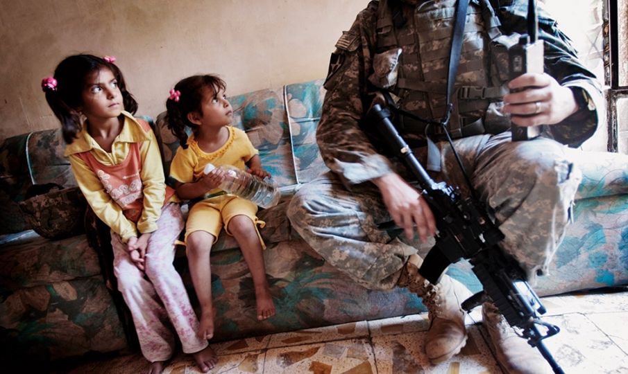 BAGHDAD, IRAQ -­ JUNE 21, 2007: Two Iraqi girls watch Staff Sgt. Nick Gibson of the 2nd Battalion, 12th Infantry Regiment of the 2nd Infantry Division as the unit was canvassing the tense Dora neighborhood. U.S. soldiers patrolled the area almost daily in an effort to get to know the residents and find insurgents. From Testament, photographs by Chris Hondros/Getty Images, text by Chris Hondros, published by powerHouse Books.