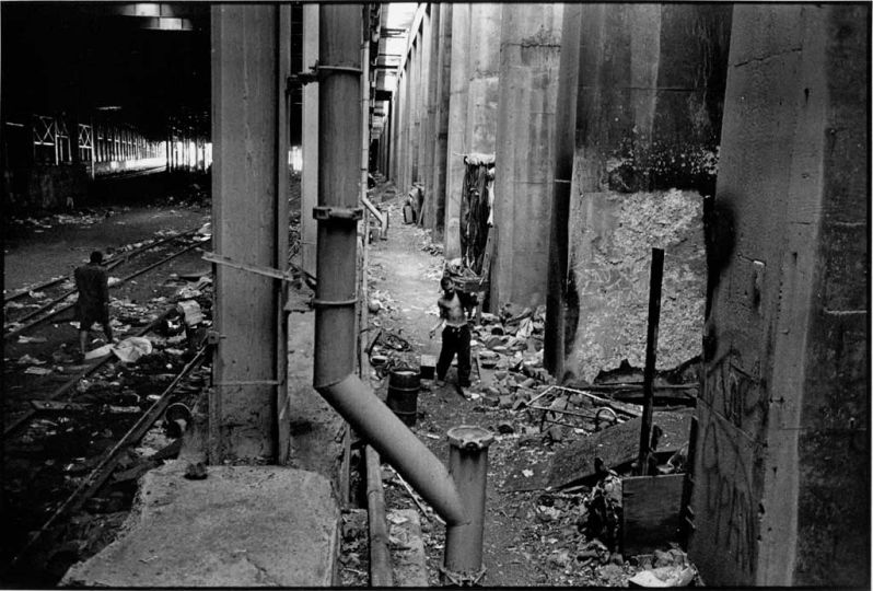 The entrance of the tunnel near 72nd Street, called 'The South End'. Tunnel dweller Poncho is leaving the tunnel, while Julio, a young man from Puerto Rico drags a record player he has found on the street to his little shack. © Teun Voeten