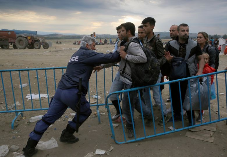 A Greek policeman pushes refugees behind a barrier at Greece's border with FYRO- Macedonia, near the Greek village of Idomeni, as thousands of migrants and refugees waited to cross September 9, 2015. REUTERS/Yannis Behrakis