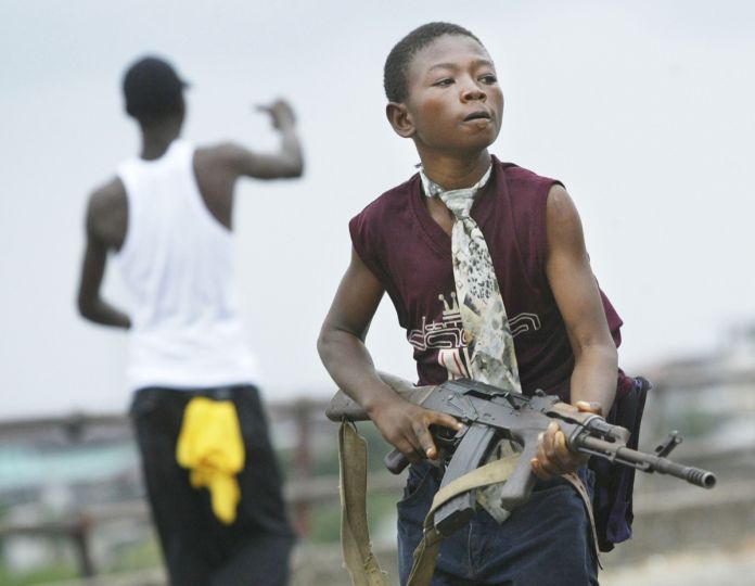 Monrovia, Liberia, July 30, 2003 - A child Liberian militia soldier loyal to the government walks away from firing while another taunts them on July 30, 2003 in Monrovia, Liberia. Sporadic clashes continue between government forces and rebel fighters in the fight for control of Monrovia. © Chris Hondros / Getty Images