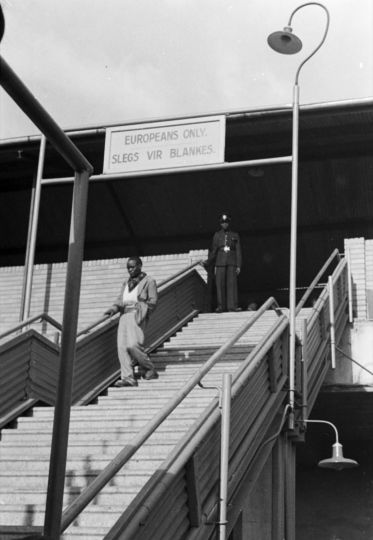 David Goldblatt, The first apartheid signs segregating facilities at Johannesburg railway station: a Black man who had used these stairs many times before is turned back after being told by a policeman that they are for 