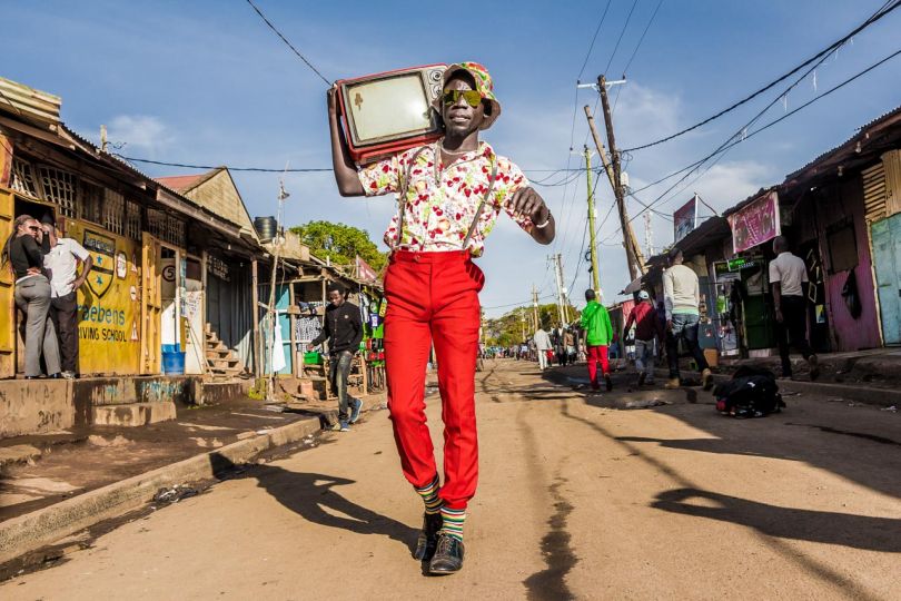 Kibera: Stories From Within © Brian Otieno 1st Place - In Kibera, a vast slum settlement located in the capital Nairobi, Kenya, Stephen Okoth also known as Ondivour is a 25 year old filmmaker, photographer and model known for his self-styled colorful and vintage fashion. He has made it his mission to stand out in bringing peace, joy and happiness to the streets of his hometown. His signature bright clothes bought from the local second-hand markets have turned him into a local personality and a source of inspiration for the youths in the slum.