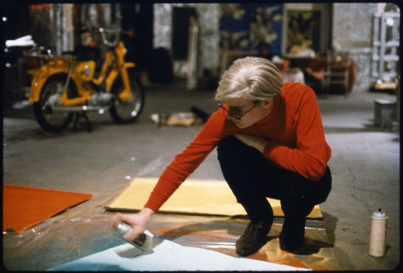 Andy Warhol with Spray Paint and Moped, The Factory, c. 1965 (Color image of Andy Warhol at work at the Factory, New York City, circa 1965) - © Nat Finkelstein Estate – Courtesy Proud Galleries