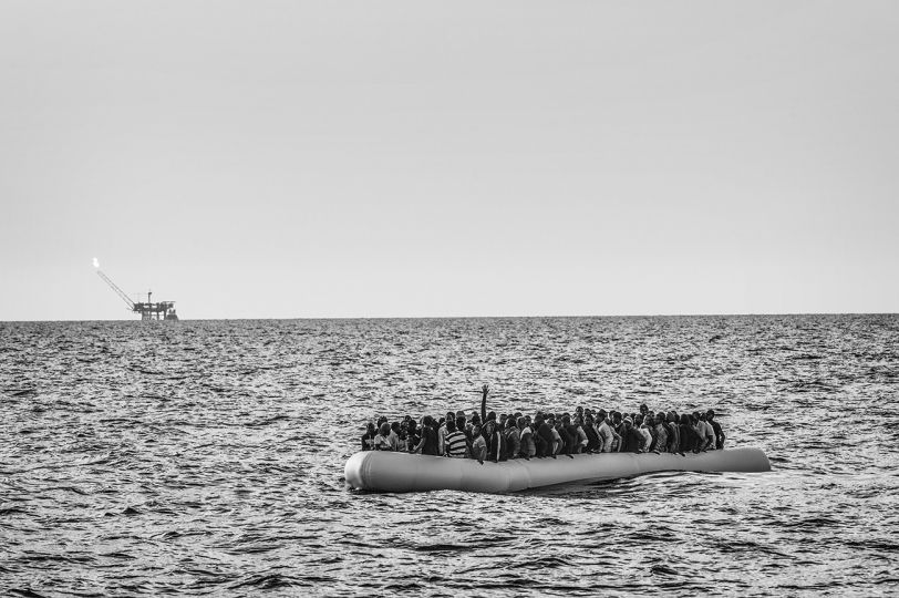 An overcrowded rubber dinghy sailed from the Libyan coast is apprached by the MSF Bourbon Argos. On the horizon, an oil platform. After the second rescue of the day, the Argos has more than 700 migrants on board. 26 August 2015. © Francisco Zizola