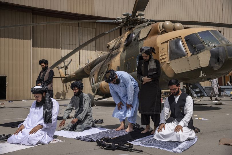 Talibs say their afternoon prayers before and MI17 helicopter damaged by departing US forces at the HKIA airport in Kabul, Afghanistan, Tuesday, August 31, 2021. This morning the final US troops left the country after 20 years of war, marking the end of America’s longest conflict and the victory of the Taliban movement. After the Talibans rapid summer advance, the US backed government collapsed on Sunday August 15, and Afghans waited nervously for their uncertain future. CREDIT: Victor J. Blue for The New York Times