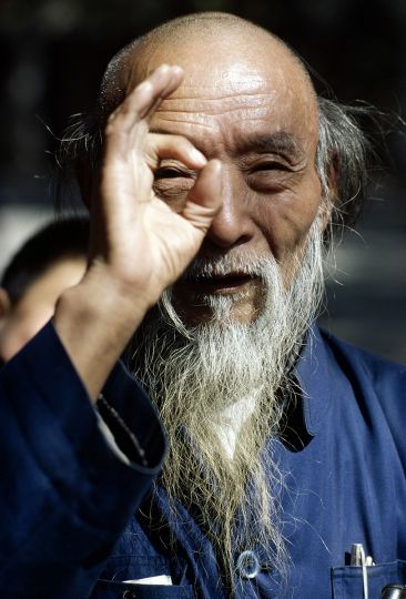 Maitre de Qi jong, Parc du Peuple, Shanghai [Il pratique un art martial, ou les deux lutteurs sont enchaines avec une corde autour du cou de moins de 1 metre. Ils doivent rendre coup pour coup, et ne peuvent fuir. Il me retourne mon acte photographique en me regardant par le trou qu'il fait avec sa main] Chine. novembre 1981. © Marc Garanger