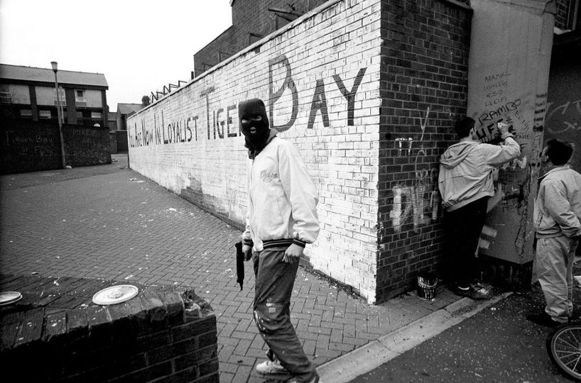 BELFAST, NORTHERN IRELAND, 1990 A hooded paramilitary gunman stands in front of a painted wall that reads “You Are Now In Loyalist Tiger Bay.” © Ed Kashi - Courtesy Kehrer Verlag