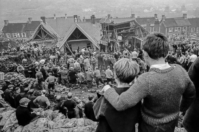 GB. WALES. 1966. Aberfan Coal Slip Disaster.  Two surviving children stand at the top of the hill overlooking the miners digging to find children still buried in the slag.  Over one hundred children in the apparent safety of their school were buried under the waste of a sliding coal tip. © David Hurn / Magnum Photos - Courtesy RRB PhotoBooks
