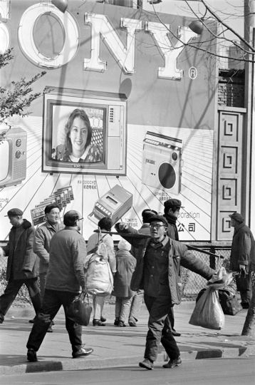 A Peasant carrying food supplies walk pass a Sony billboard on the busy Nanjing Road in Shanghai,1982. © HS Liu