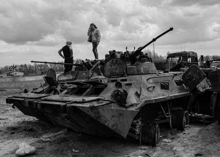 Local teens play on a destroyed Russian tank that has been placed in a junkyard which over that past few weeks has become a “tank graveyard” in Bucha weeks after Russian forces were pushed out of the area on April, 2022. © Byron Smith - From the book Testament ’22 - Courtesy Verlag Kettler
