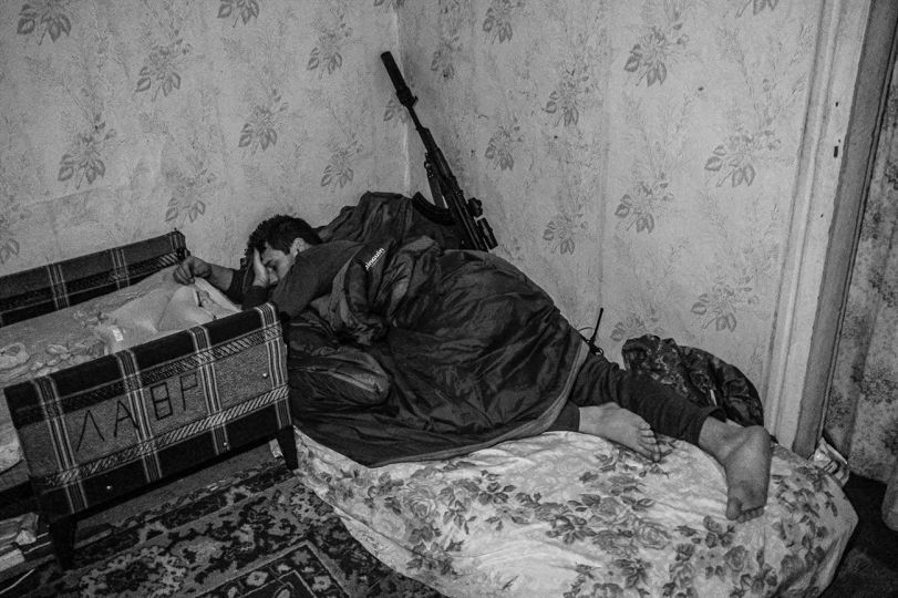 Five kilometers from the Ukrainian-Russian border in the Kharkiv region, a Ukrainian special forces soldier with the 130 Battalion out of Kyiv sleeps in amid artillery and heavy weapons fire with his squad at a safe house. The previous day he and his team provided “security” to enable a mining squad to carry out their mission between the Ukrainian and Russian frontlines. November, 2022. © Byron Smith - From the book Testament ’22 - Courtesy Verlag Kettler