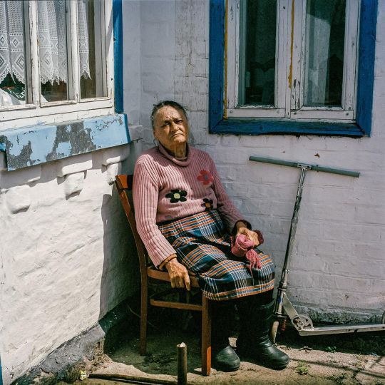 Tetyana, an 81-year-old blind woman sits outside of her home which had just liberated from Russian occupation. Andriivka, May, 2022. © Byron Smith - From the book Testament ’22 - Courtesy Verlag Kettler