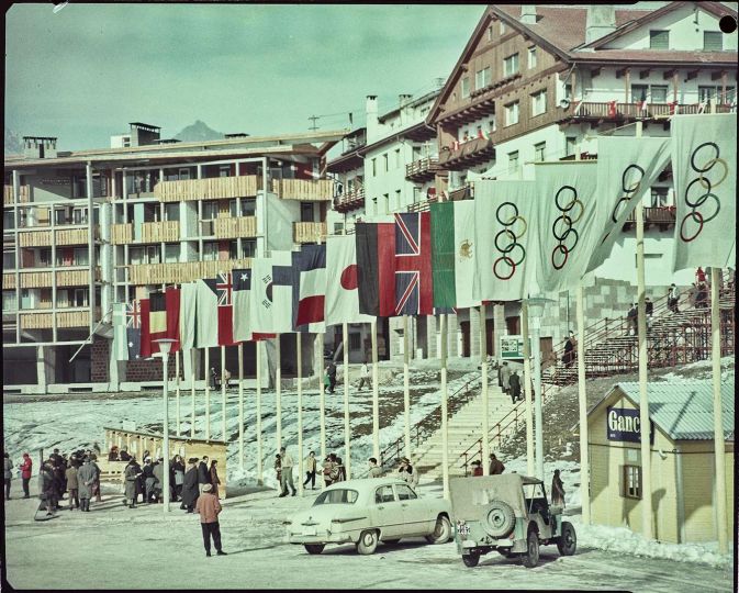 Flags of various countries and of the five Olympic rings on display in Cortina d'Ampezzo, January-February 1956. Photograph by Publifoto. Intesa Sanpaolo Publifoto Archive. The road to Cortina. 7th Winter Olympic Games exhibition