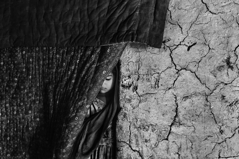Kabul, Afghanistan, March 2019: A girl stands at the entrance of her family’s mud house in the Hussain Khail informal settlement. Her uncle and brother were killed in their compound during an airstrike in the village of Chardara. Survivors were trapped in the crossfire between the Taliban and the Afghan Army for an entire day before they were evacuated to Kabul during a lull in the fighting. The family never returned to their house after the incident. © Lorenzo Tugnoli